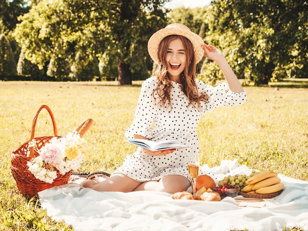 Young beautiful hipster woman in trendy summer sundress and hat. Carefree woman making picnic outside. 