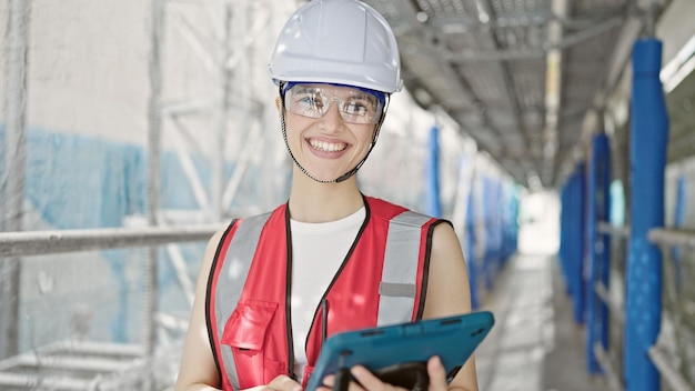 Young beautiful hispanic woman builder smiling confident using touchpad at street