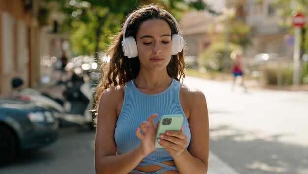 Young beautiful hispanic woman watching video on smartphone at street