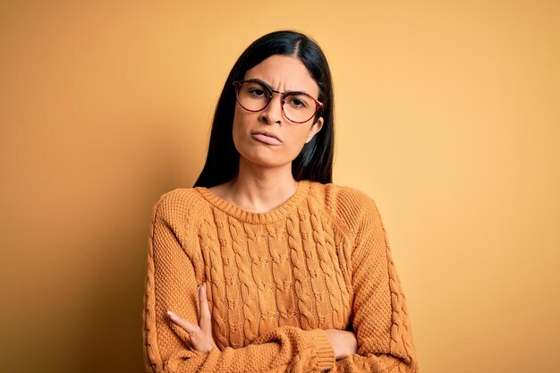 黄色の孤立した背景の上に眼鏡をかけている若い美しいヒスパニック系女性