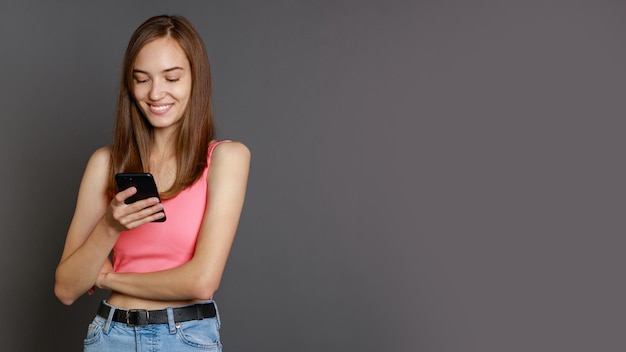 Молодая красивая дама играет со своим телефоном на сером фоне
