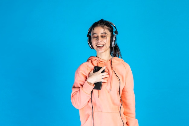 Young beautiful lady put her phone to her chest and listening music on blue background