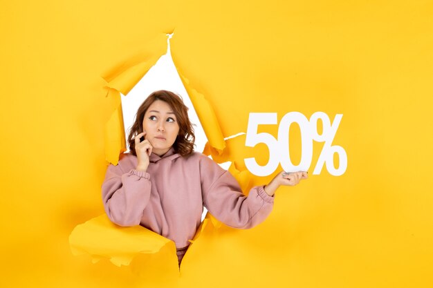 Young beautiful lady showing fifty percentage sign and feeling surprised on yellow torn breakthrought background