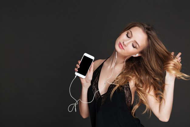 Young beautiful lady showing phone display and listening music