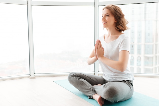 Young beautiful lady sitting near window make yoga exercises.