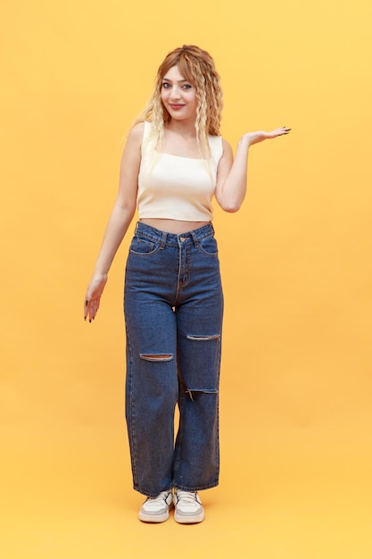 Young beautiful lady standing on orange background and holding her hand open while looking at the camera