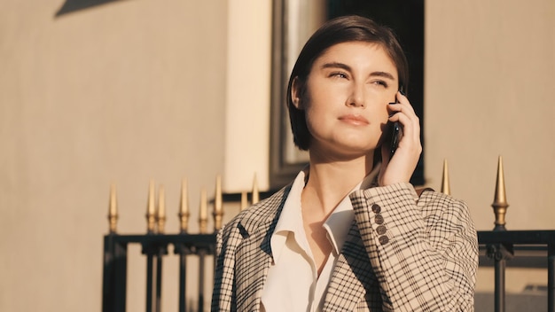 Young beautiful lady talking on smartphone waiting business meet on city street. Always in touch