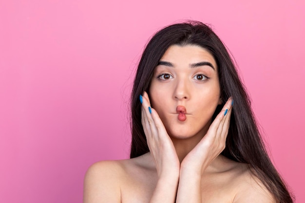 Young beautiful lady WinCo her lips and looking at the camera on pink background High quality photo