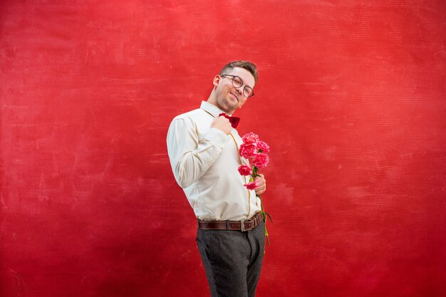 Young beautiful man with flowers on red studio background