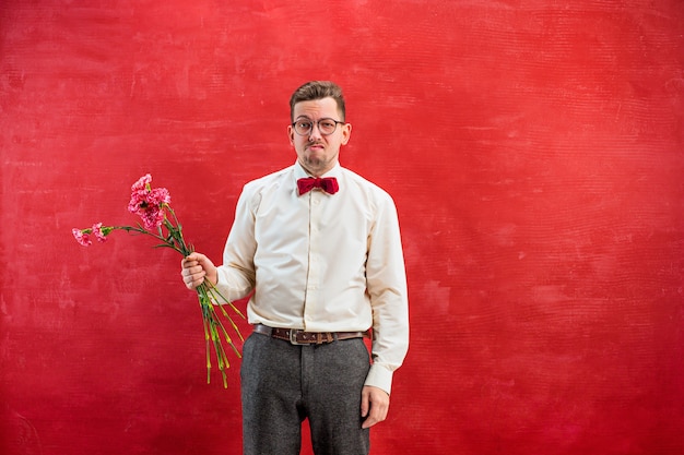 Young beautiful man with flowers on red studio background