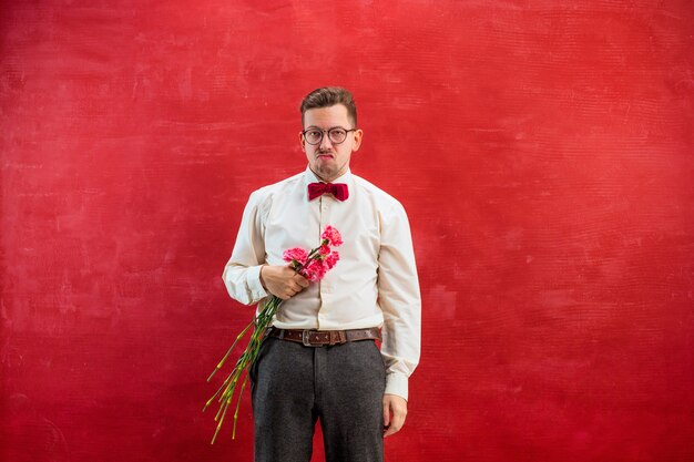 Young beautiful man with flowers on red studio