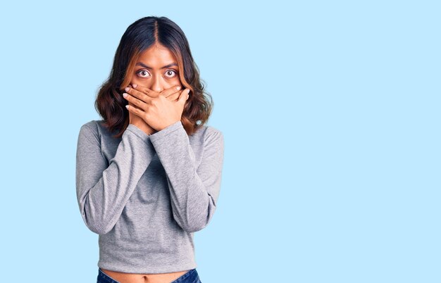 カジュアルな服を着た若い美しい混血の女性は、間違いのために口を手で覆ってショックを受けました。秘密のコンセプト。