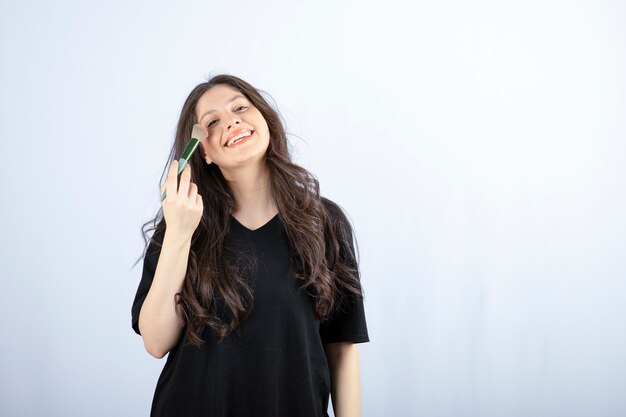 young beautiful model applying shadow with brush on white wall. 