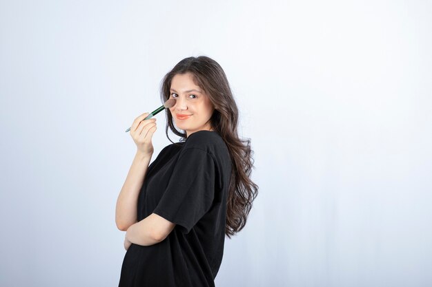 young beautiful model applying shadow with brush on white wall. 