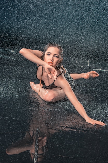 La giovane bella ballerina moderna danza sotto le gocce d'acqua