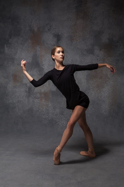 Молодая красивая танцовщица современного стиля позирует на сером фоне студии