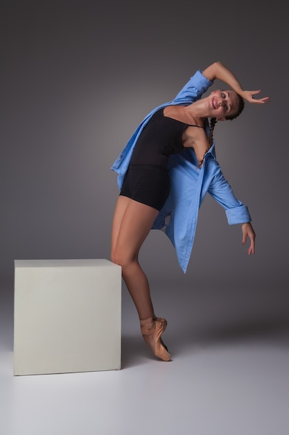 The young beautiful modern style dancer posing on white cube on a studio gray background