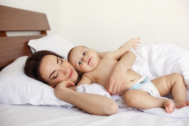 닫힌 된 눈과 그녀의 신생아 이른 아침 침대에 누워있는 젊은 아름 다운 어머니.