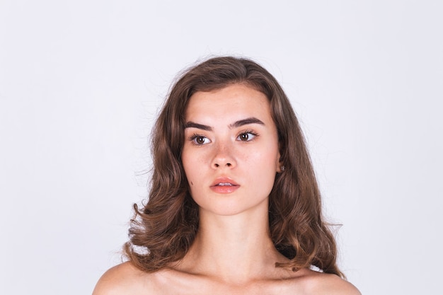 Free photo young beautiful natural soft clean skin woman with freckles light makeup on white wall with bare shoulders