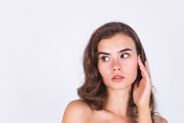 Young beautiful natural soft clean skin woman with freckles light makeup on white wall with bare shoulders