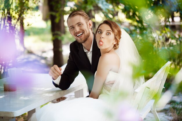 Young beautiful newlyweds fooling, sitting in cafe outdoors.