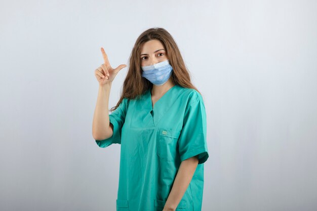 上向きの医療マスクで緑の制服を着た若い美しい看護師