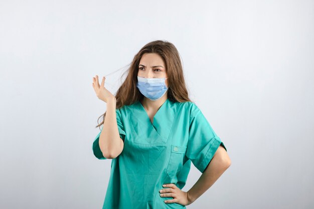 医療マスクを身に着けている緑の制服を着た若い美しい看護師