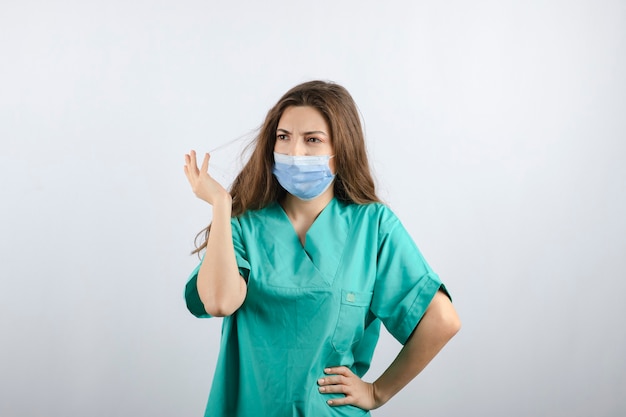 의료 마스크를 쓰고 녹색 제복을 입은 젊은 아름다운 간호사