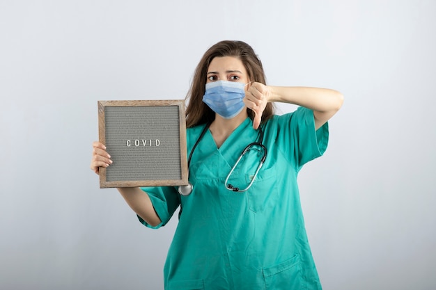 Молодая красивая медсестра в медицинской маске с рамкой, показывающей большой палец вниз