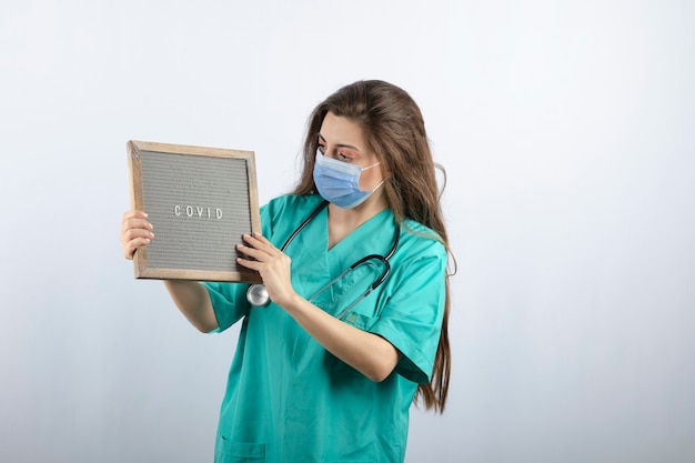 Young beautiful nurse in medical mask with stethoscope holding a frame 