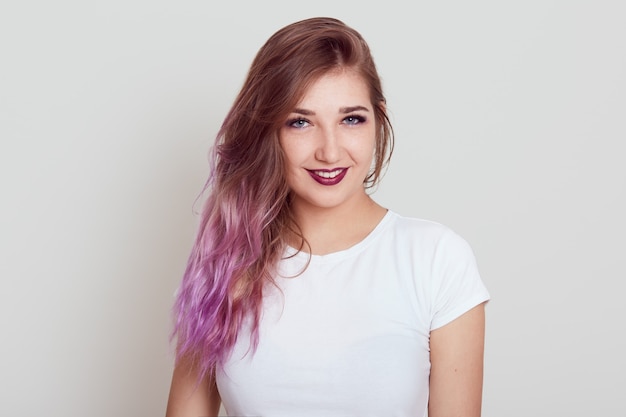 Young beautiful self confident lady in white casual t shirt and expressing positive emotions, sees something pleasant, posing isolated over gray wall.