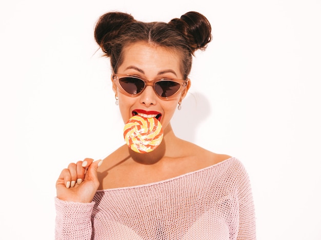 Young beautiful sexy hipster woman with red lips in sunglasses.trendy girl in summer swimwear clothes. eating,biting candy lollipop