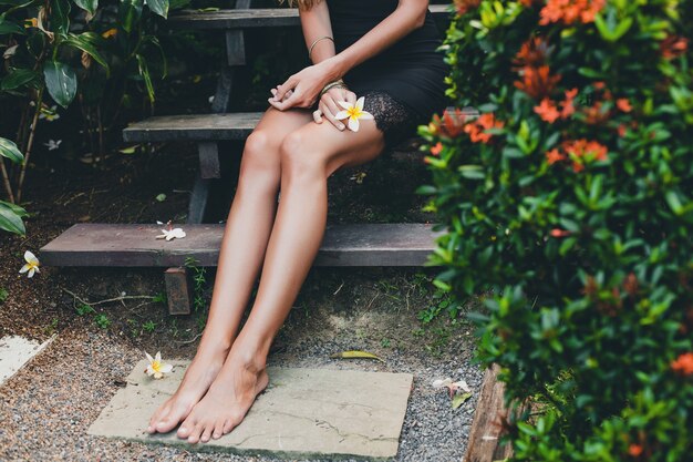 Young beautiful sexy woman in tropical garden, summer vacation in thailand, slim skinny tanned body, little black dress with lace, natural look, sensual, relaxed, legs close up details