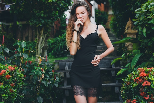Молодая красивая сексуальная женщина в тропическом саду, летние каникулы в Таиланде, стройное худое загорелое тело, маленькое черное платье с кружевом, естественный вид, чувственный, расслабленный,