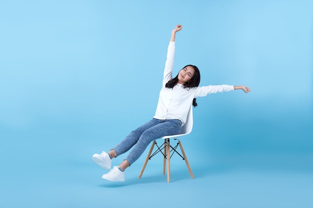 Young beautiful smiling asian girl relaxing sitting on chair on blue.