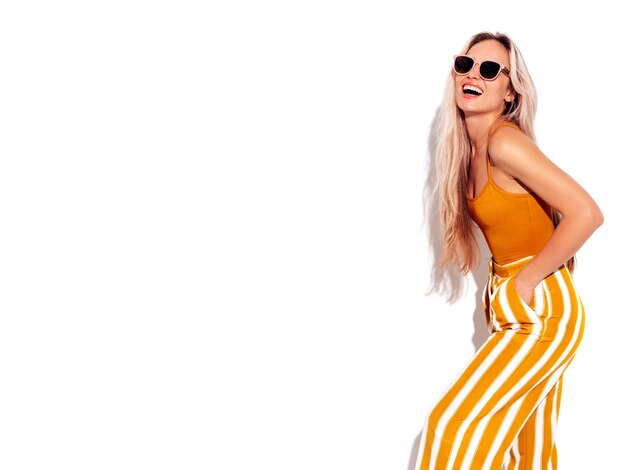 Молодая красивая улыбающаяся блондинка в модной летней желтой одежде Сексуальная беззаботная женщина, изолированная на белом в студии Позитивная модель веселится в помещении Веселая и счастливая В солнцезащитных очках