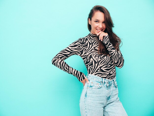 Young beautiful smiling female in trendy summer clothes carefree woman posing near wall in studio Positive brunette model having fun Cheerful and happy