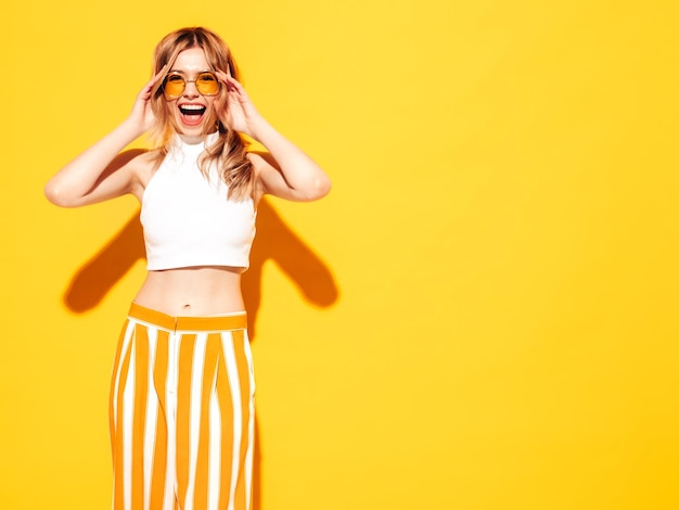 Free photo young beautiful smiling female in trendy summer clothes sexy carefree woman posing near blue yellow in studio positive model having fun cheerful and happy in sunglasses screaming and shouting