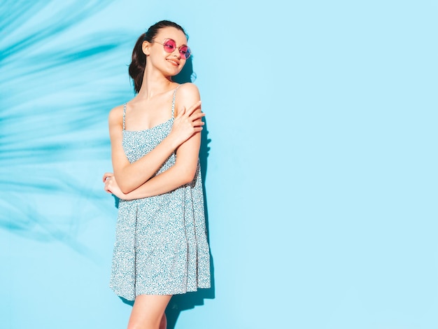 Молодая красивая улыбающаяся женщина в модном летнем платье Сексуальная беззаботная женщина позирует возле синей стены в студии Позитивная брюнетка-модель веселитсяВеселая и счастливая Изолированная