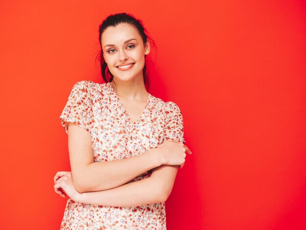 Young beautiful smiling female in trendy summer dress Sexy carefree woman posing near red wall in studio Positive brunette model having fun and going crazy Cheerful and happy