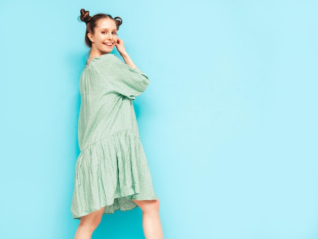 Free photo young beautiful smiling female in trendy summer green dress sexy carefree woman with two horns hairstyle posing near blue wall in studio positive model having fun cheerful and happy