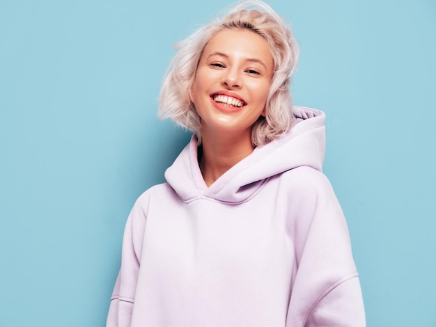 Free photo young beautiful smiling female in trendy summer hoodie sexy carefree woman posing near blue wall in studio positive blond model having fun and going crazy cheerful and happy