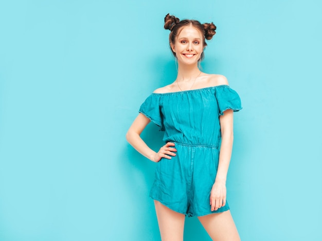 Young beautiful smiling female in trendy summer jeans overalls Sexy carefree woman with two horns hairstyle posing near wall in studio Positive model having fun Cheerful and happy Isolated