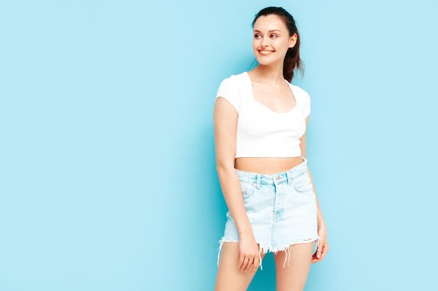 Young beautiful smiling female in trendy summer jeans skirt and top clothes Sexy carefree woman posing near blue wall in studio Positive brunette model having funCheerful and happy