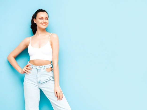 Free photo young beautiful smiling female in trendy summer jeans and top clothes sexy carefree woman posing near blue wall in studio positive brunette model having funcheerful and happy
