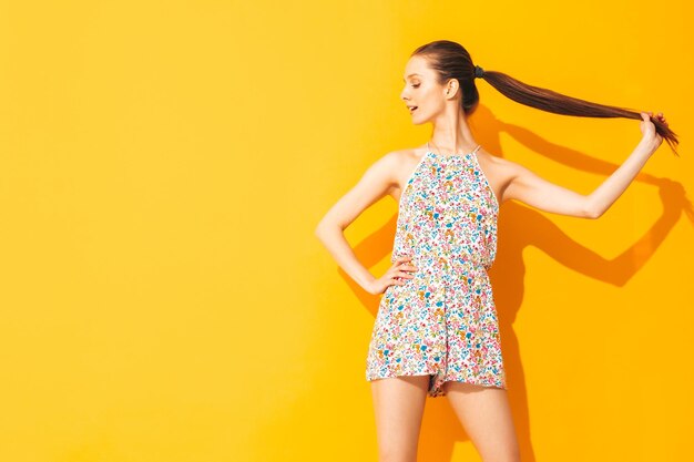 Young beautiful smiling female in trendy summer overalls Sexy woman with posing near yellow wall in studio Positive model having fun Cheerful and happy