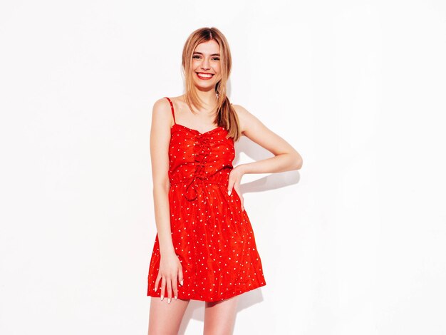 Young beautiful smiling female in trendy summer red dress Sexy carefree blond woman posing near white wall in studio Positive model having fun Cheerful and happy Isolated