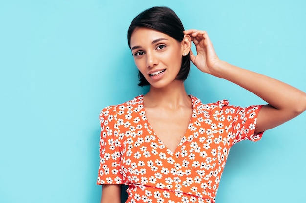 Free photo young beautiful smiling female in trendy summer red dress sexy carefree woman posing near blue wall in studio positive model having fun cheerful and happy isolated