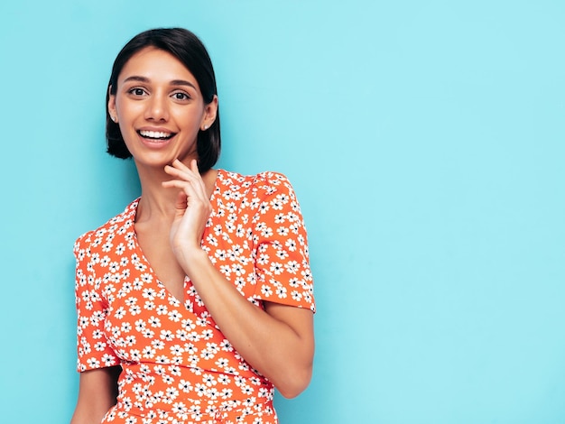 Free photo young beautiful smiling female in trendy summer red dress sexy carefree woman posing near blue wall in studio positive model having fun cheerful and happy isolated