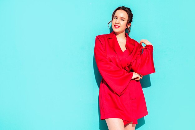 Young beautiful smiling female in trendy summer red dress Sexy carefree woman posing near blue wall in studio Positive model having fun Cheerful and happy